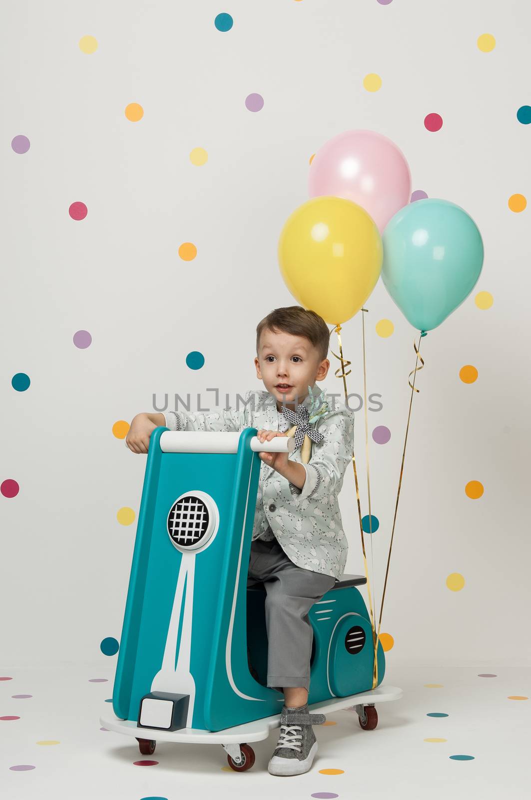 Boy in costume designer on a toy bike with balloons on a white background