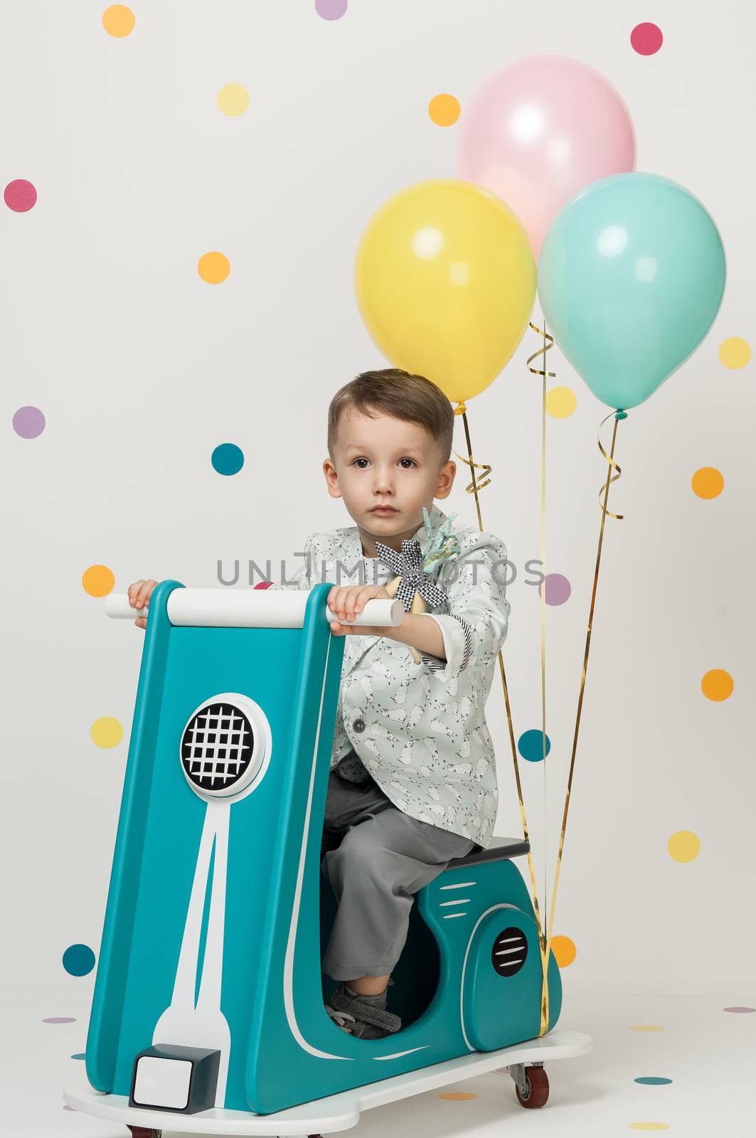 Boy in costume designer on a toy bike with balloons on a white background