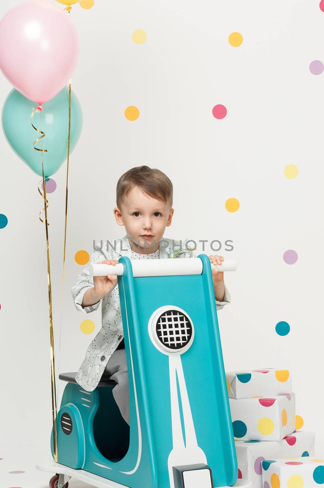 Boy in costume designer on a toy bike with balloons on a white background