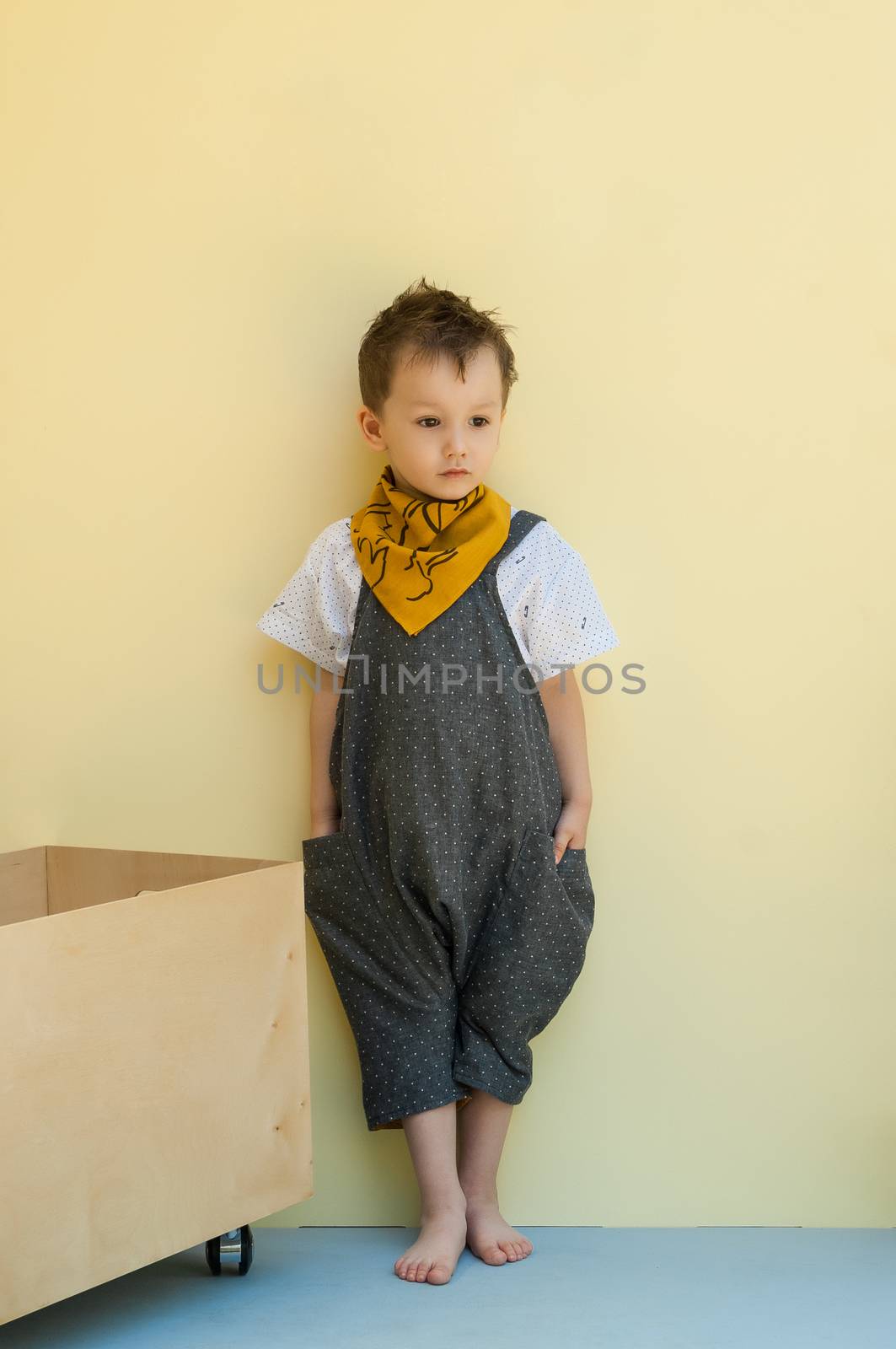 little boy in a jumpsuit with a wooden box on a yellow background