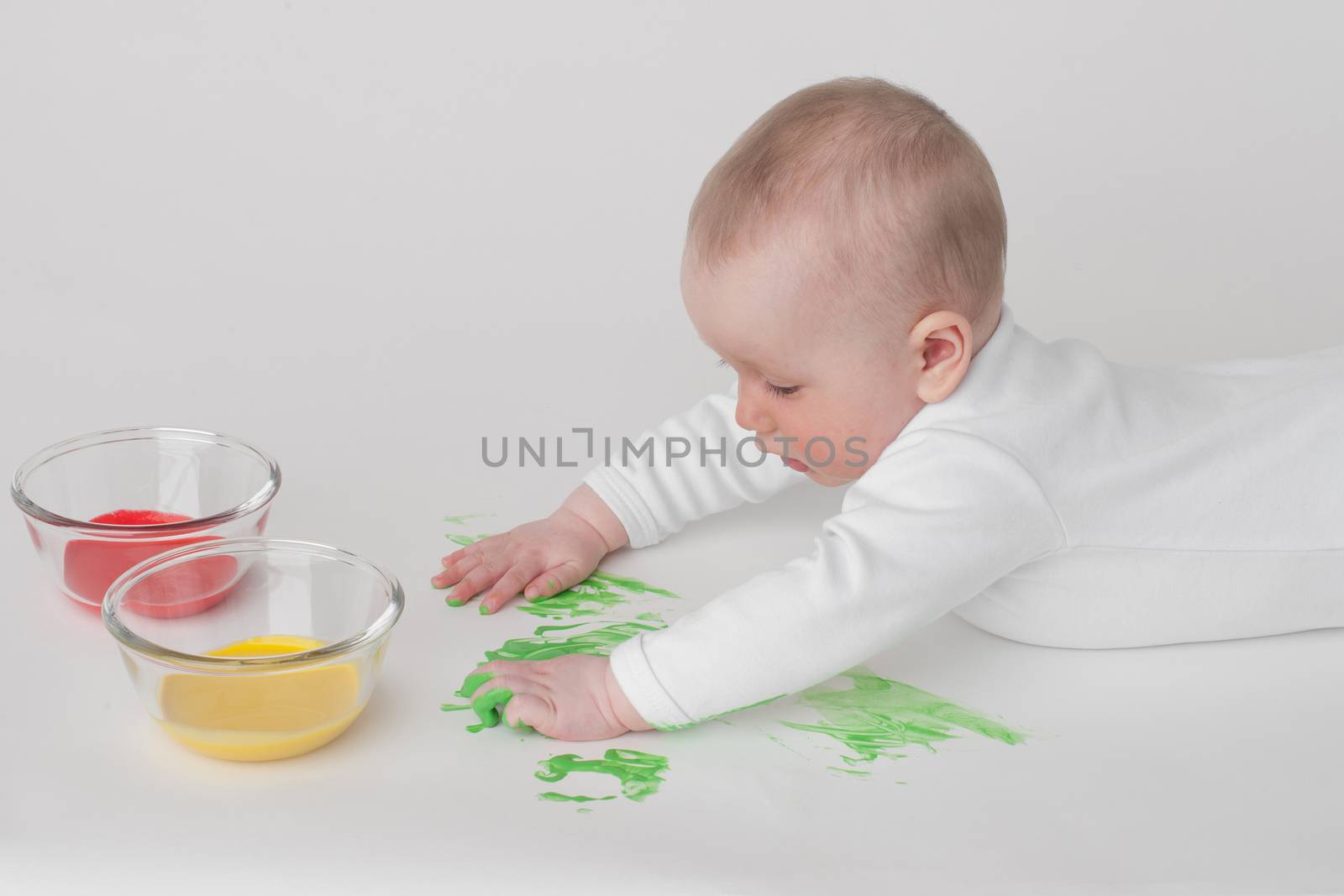 baby on a white background in a white pajamas with paints