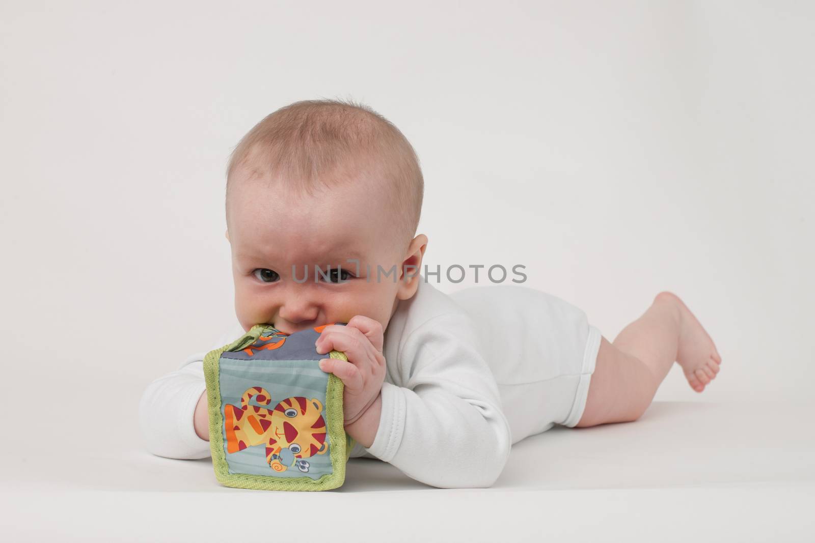 baby on a white background in a white pajamas with toy cube