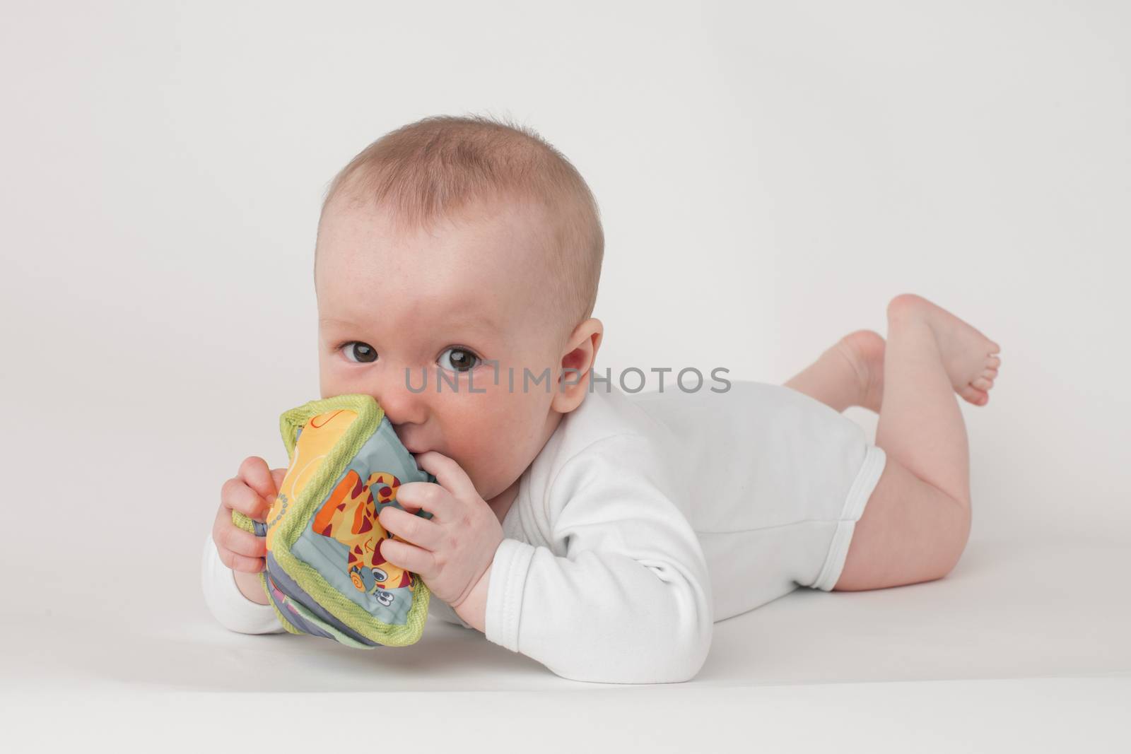 baby on a white background in a white pajamas with toy cube