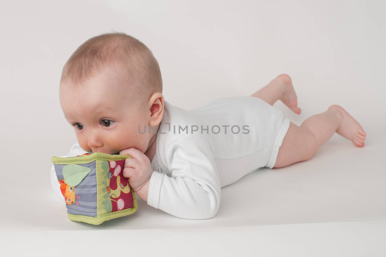 baby on a white background in a white pajamas with toy cube