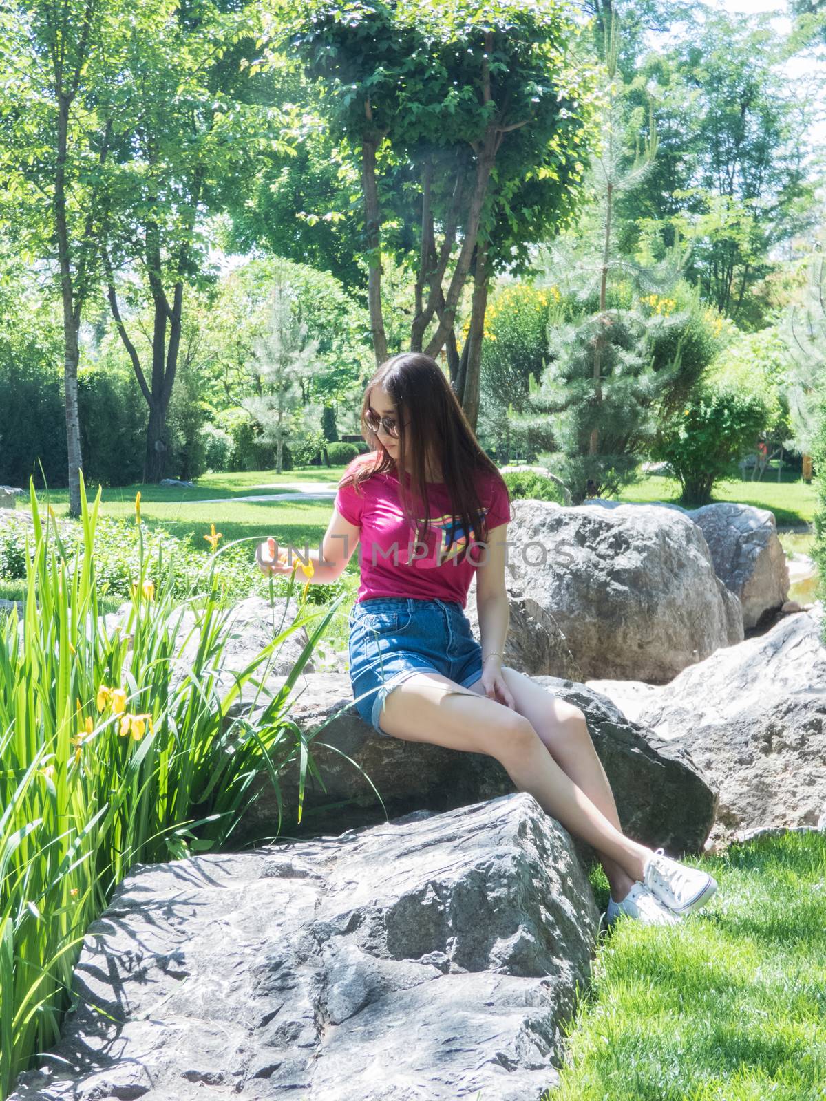 a young girl is sitting on a large rock in a picturesque park in sunny day. the girl of Asian appearance