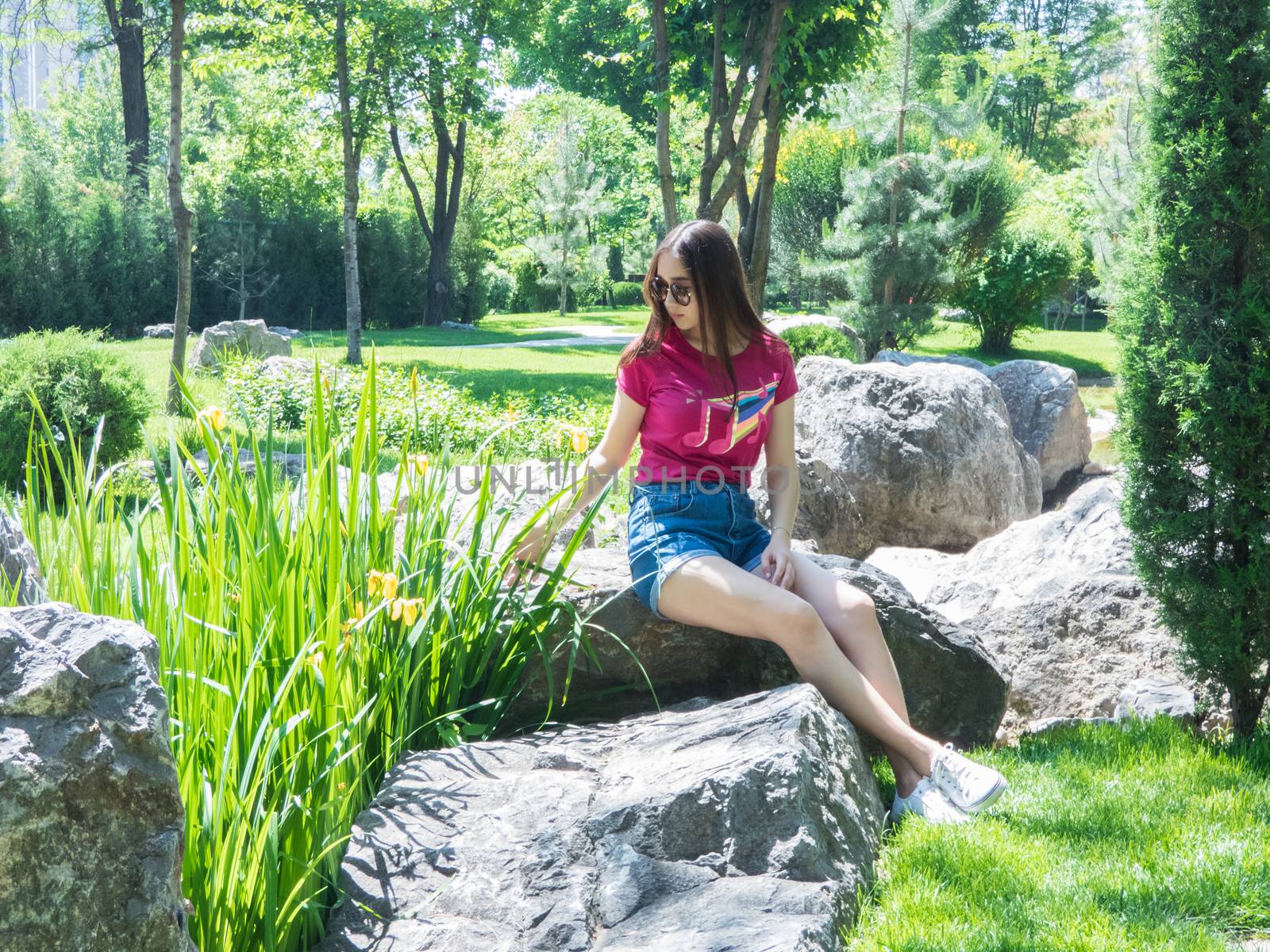 a young girl is sitting on a large rock in a picturesque park in sunny day. the girl of Asian appearance