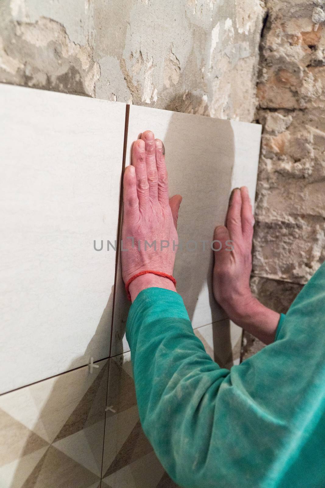 The worker puts tiles on the wall. Finishing works, blurred focus. The technology of laying tile.