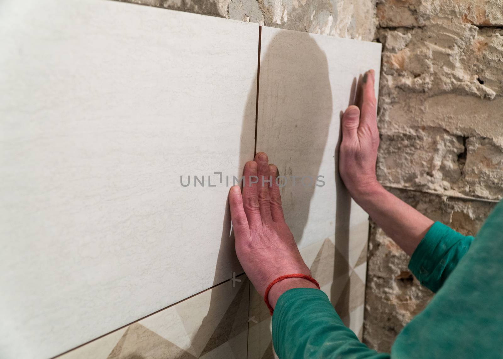 The worker puts tiles on the wall. Finishing works, blurred focus. The technology of laying tile.