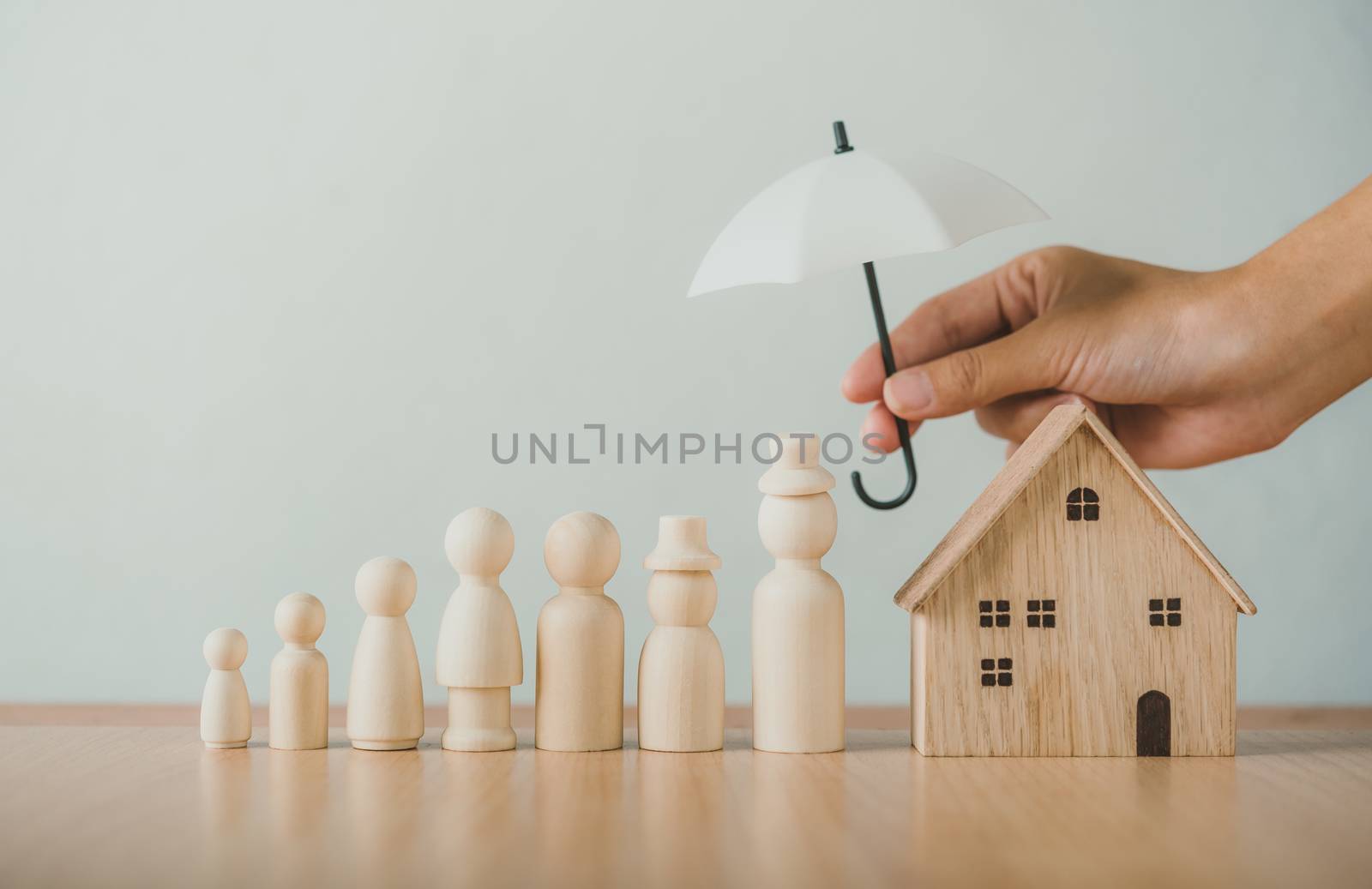 Hands holding umbrellas on wooden puppets, family and home . Life insurance concept, family protection care Family safety