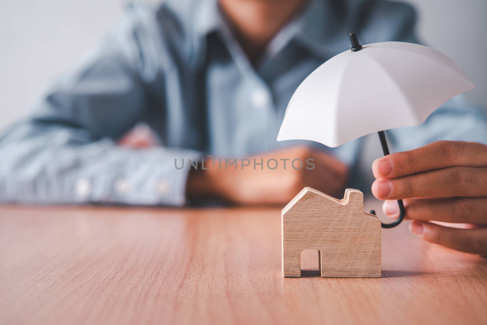 Hands holding an umbrella on a wooden house. Concept of home ins by photobyphotoboy