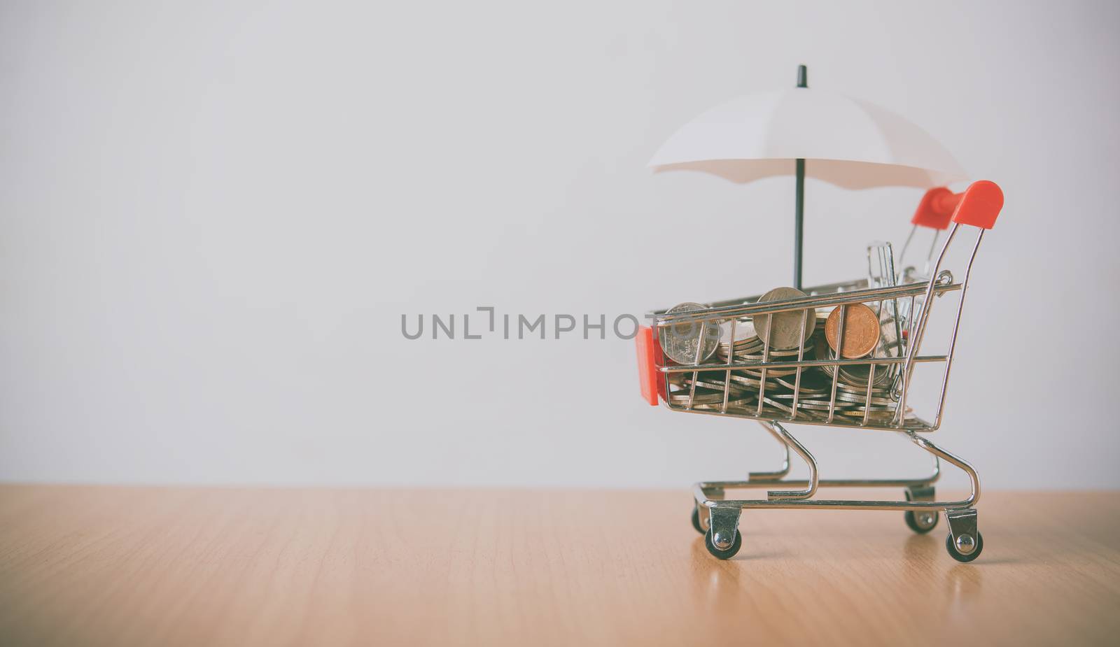 Umbrella is on the currency, the coin is in a shopping cart that is placed on the wooden floor. The concept of protection and protection and safety supervision in business