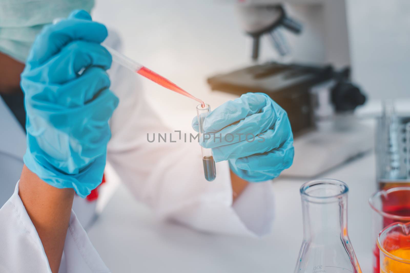  Female researchers are experimenting with pipette dropping a sample into a test tube in an experiment research in laboratory.
