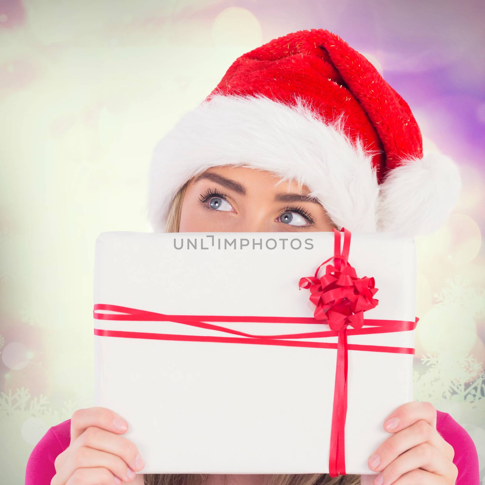 Festive blonde holding christmas gift against glowing christmas background