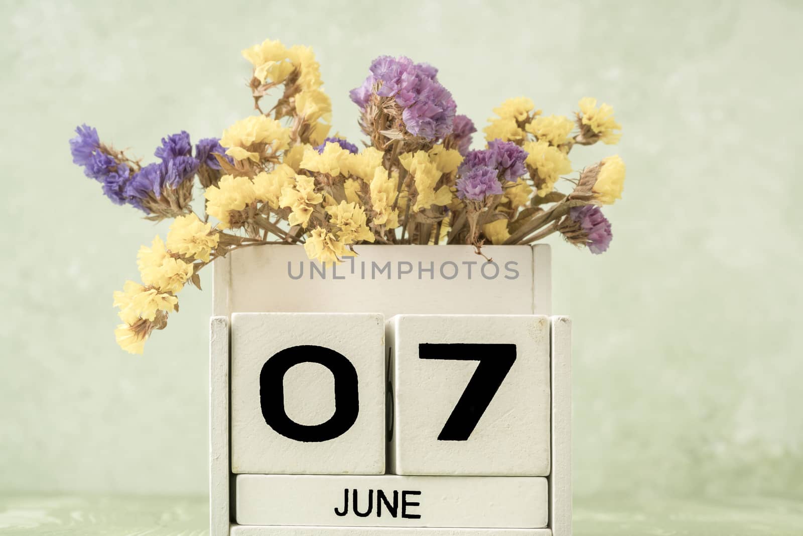 White cube calendar for june decorated with flowers over green background with copy space
