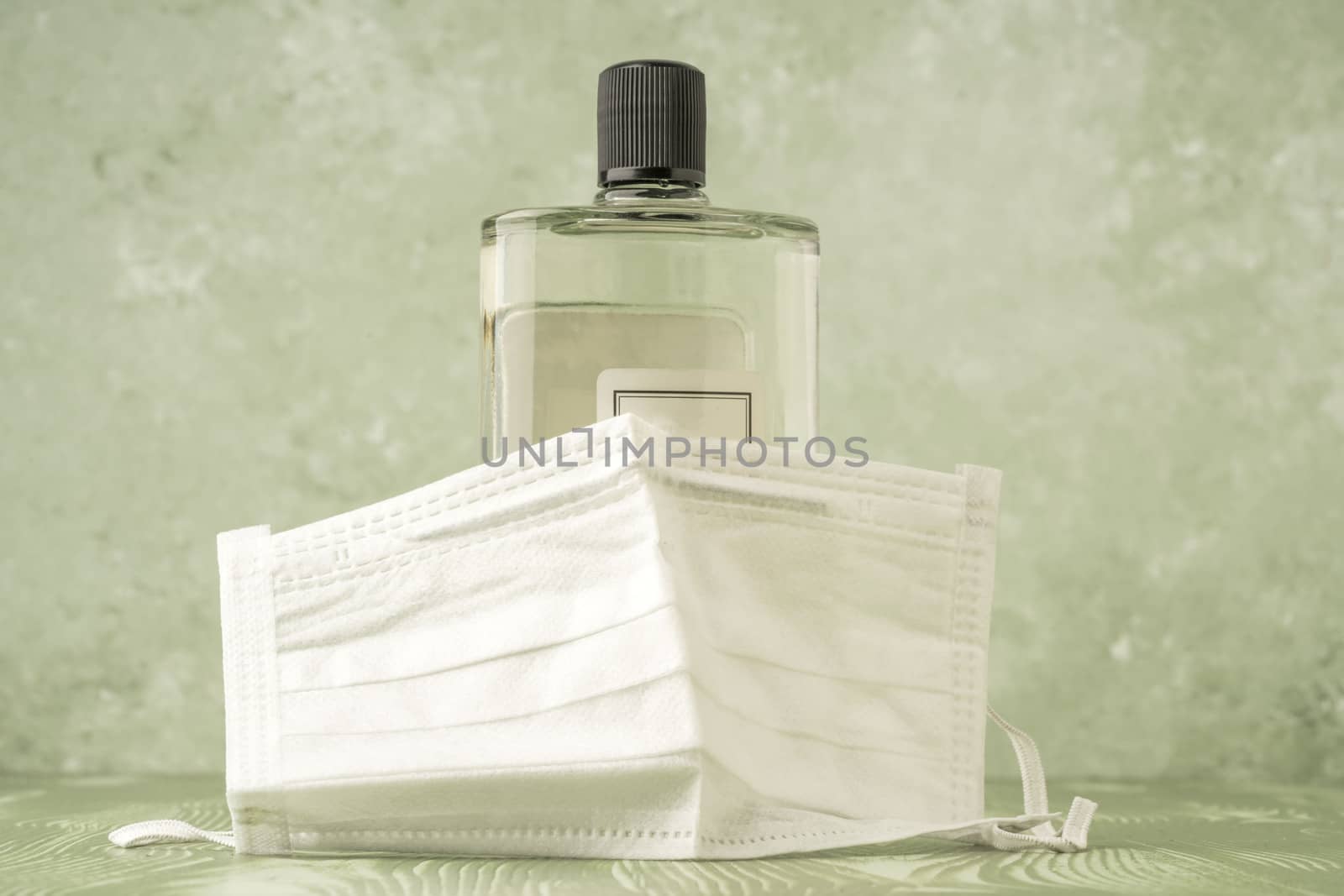bottle of cologne covered with a disposable health mask over green with copy space