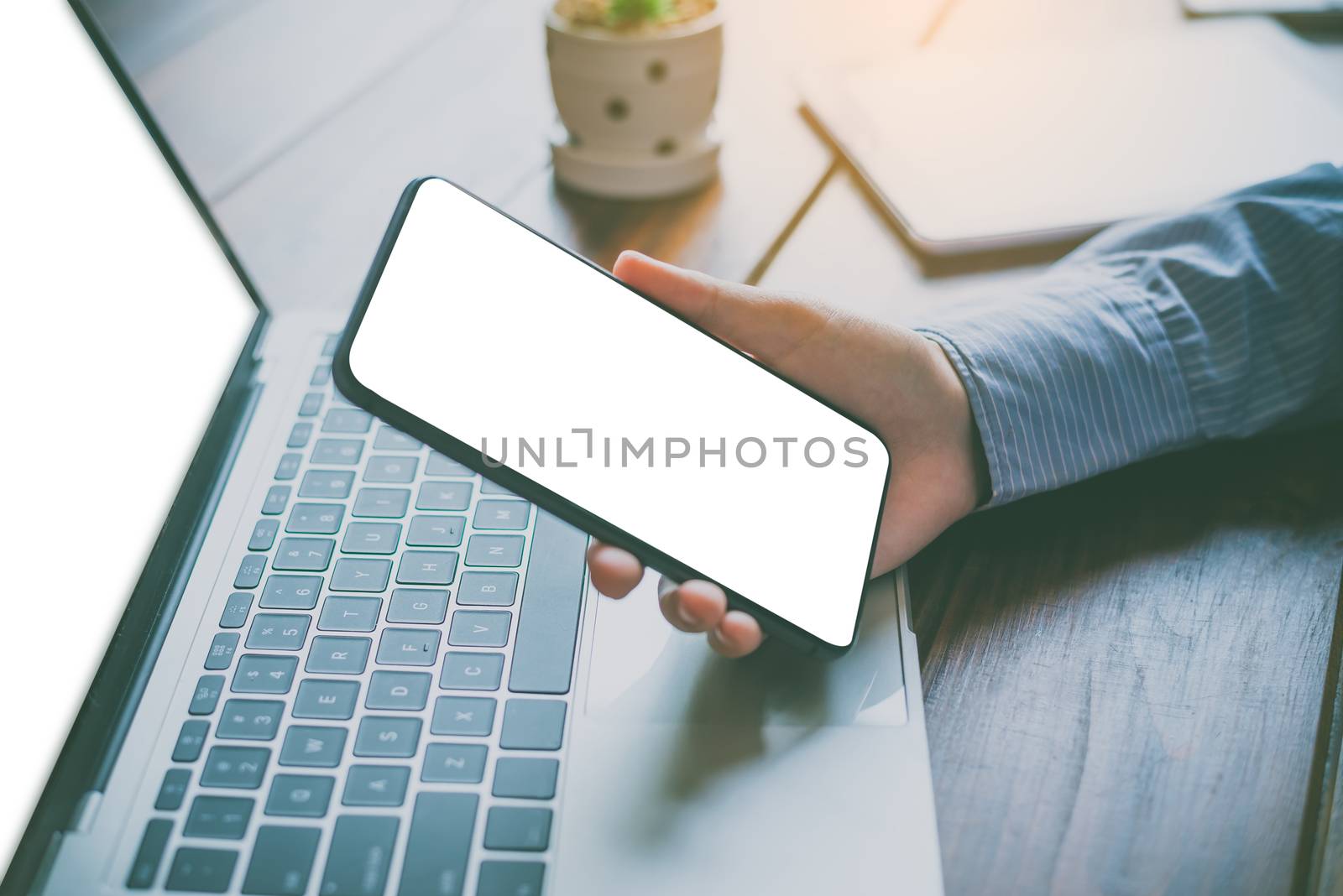 close-up mockup image of  hand holding black mobile phone with blank white  in desk work for home.