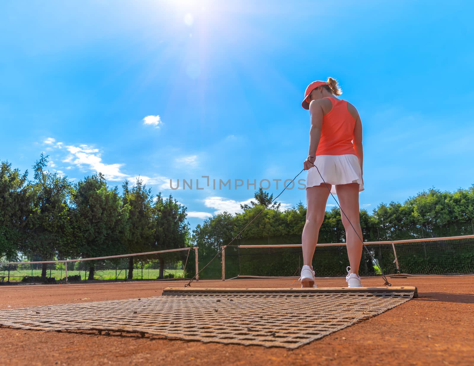 sweeping orange clay on an outdoor tennis court. young woman by Edophoto