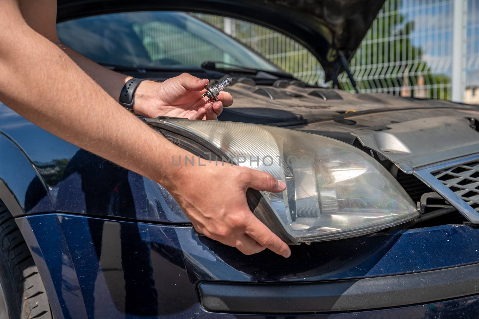 The man changes the bulb in the headlight of a car.