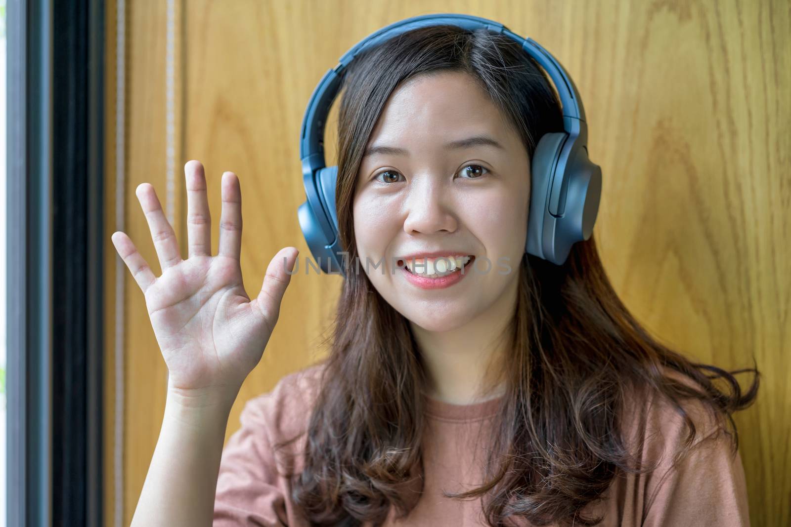 Asian Young woman waving hand for say hello when making video call to friend with social distancing, smiling female taking video blog recording vlog, Covid-19 pandemic, headphone and online meeting