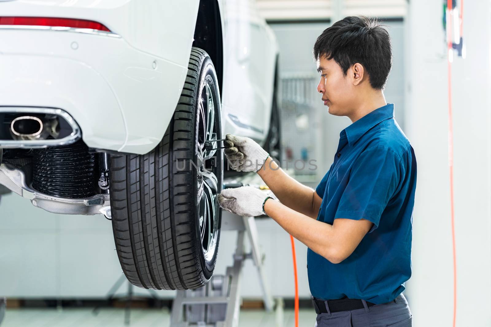 Asian mechanic checking and repairing the car wheels in maintain by Tzido