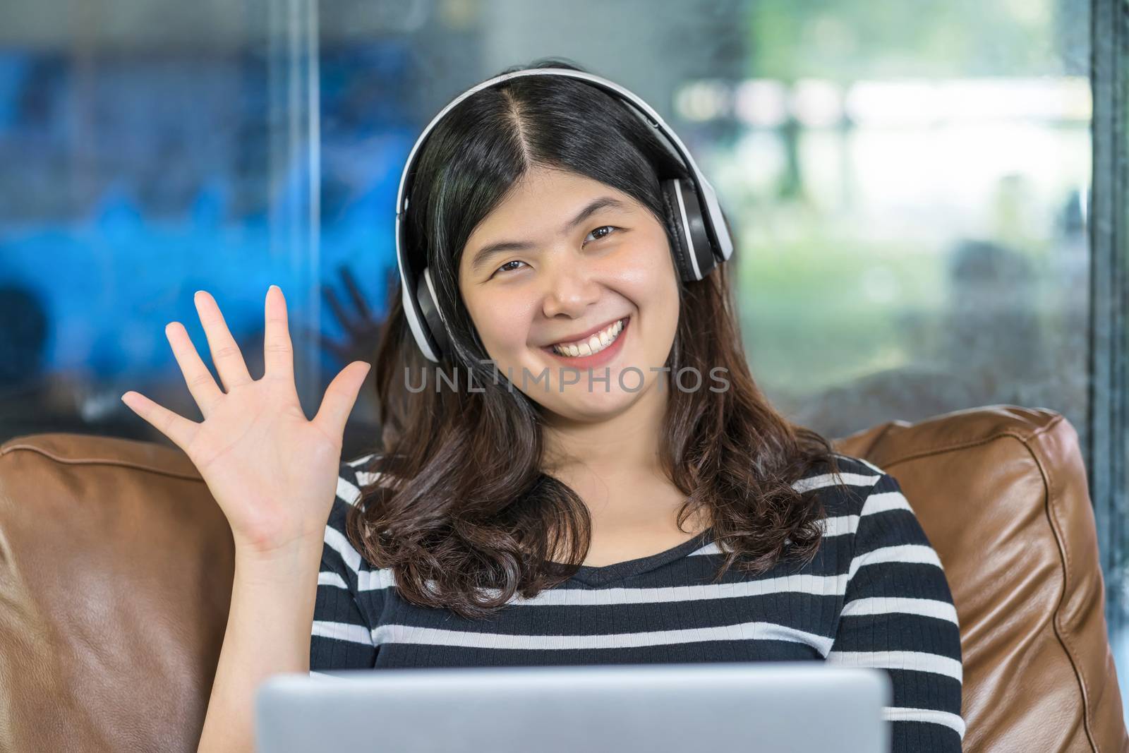Asian business woman waving hand for say hello when making video call to friend with social distancing, smiling female taking video blog recording vlog, Covid-19 pandemic, headphone and online meeting