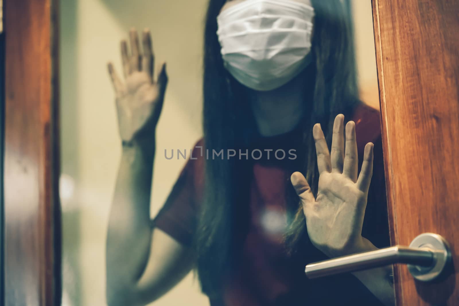 Closeup hand of Asian woman wearing medical mask touching Glass door when stay isolation at home for self quarantine in Covid-19 outbreak situation, coronavirus pandemic and lockdown,Social distancing