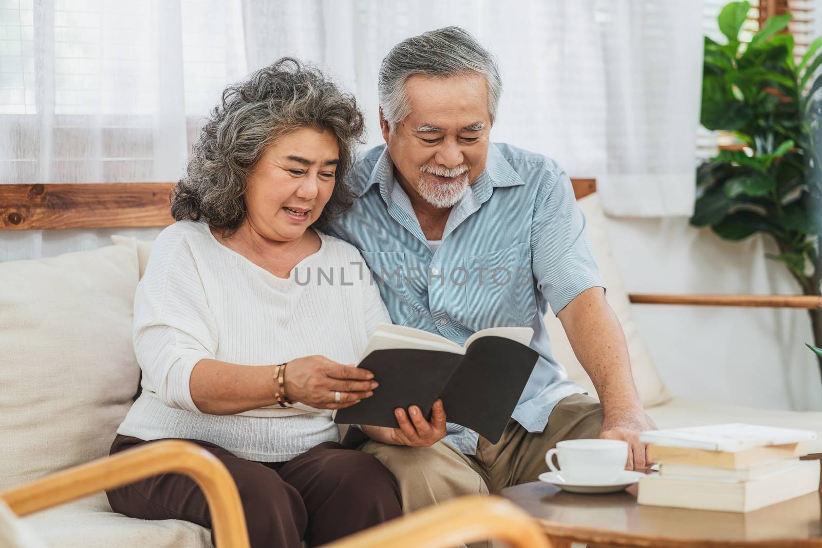 Asian couple Grandparent sitting and reading the book together with happy feeling in house, Long live and Elderly society, Warm family and happiness, covid19 outbreak and social distancing concept
