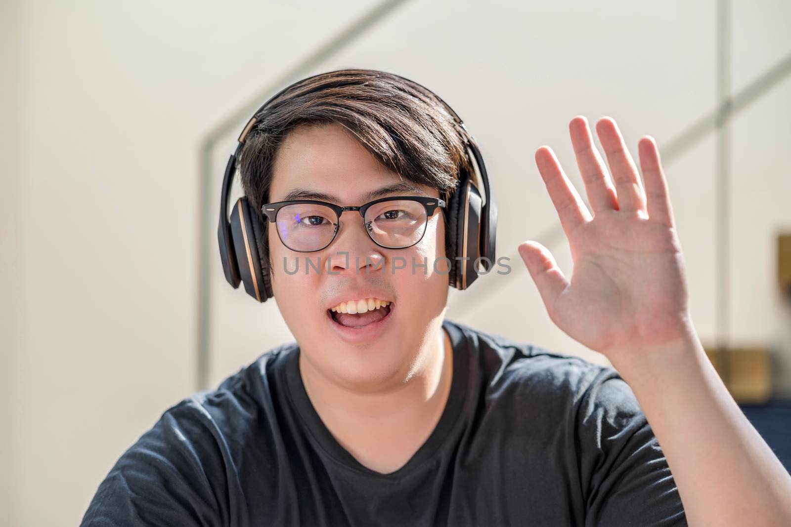 Asian business man waving hand for say hello when making video call to friend with social distancing, smiling female taking video blog recording vlog, Covid-19 pandemic, headphone and online meeting