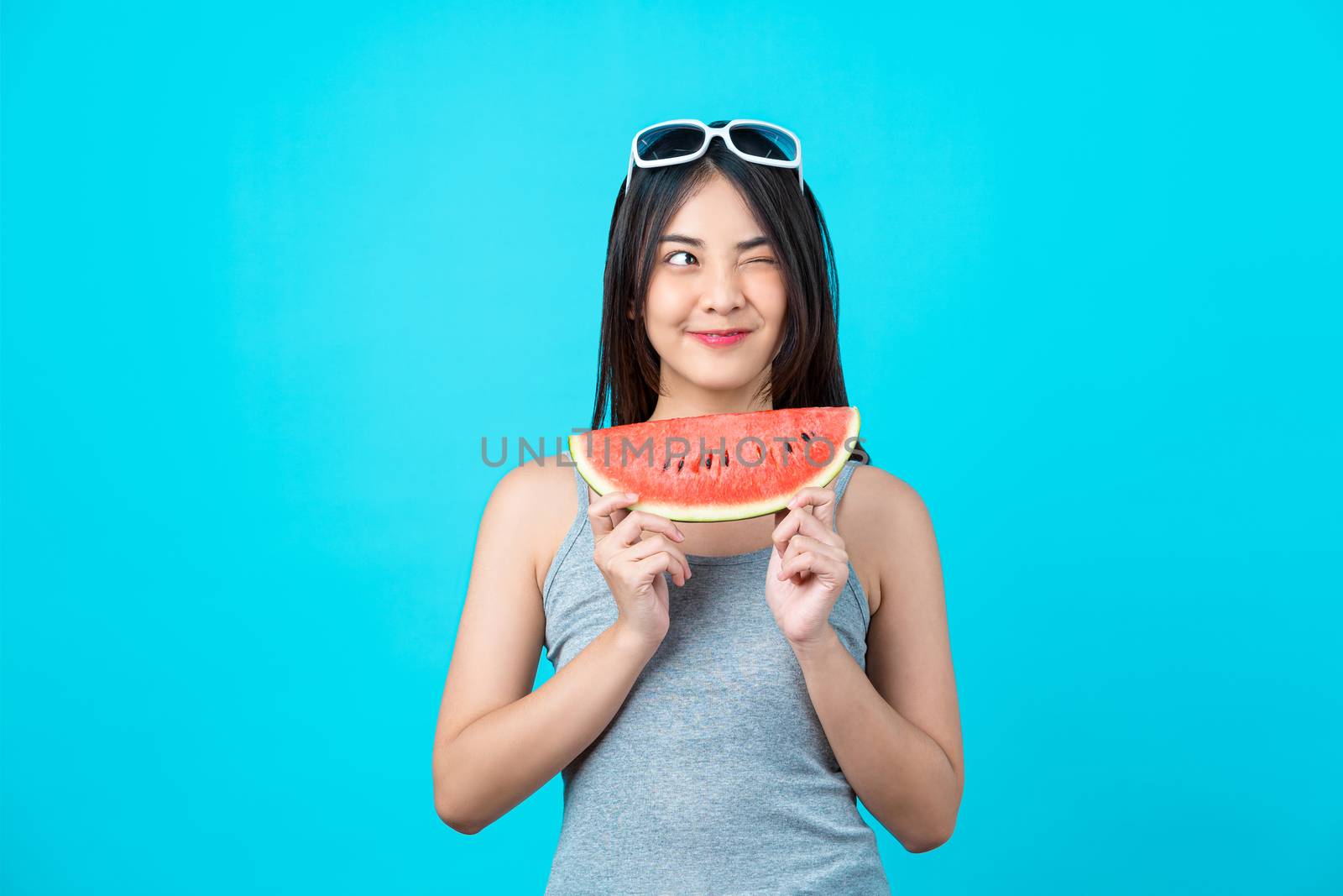 Attractive Asian young woman wearing summer vest and holding the Piece slide of watermelon on isolated blue color background, Sexy mouth bite, copy space and studio, fashion travel and tourist concept