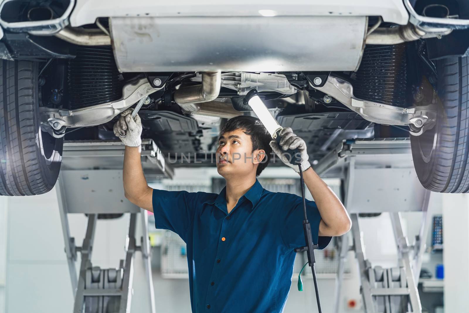 Closeup Asian mechanic hand repairing under the car in maintainance  service center which is a part of showroom, technician or engineer professional work for customer, car repair and maintain concet