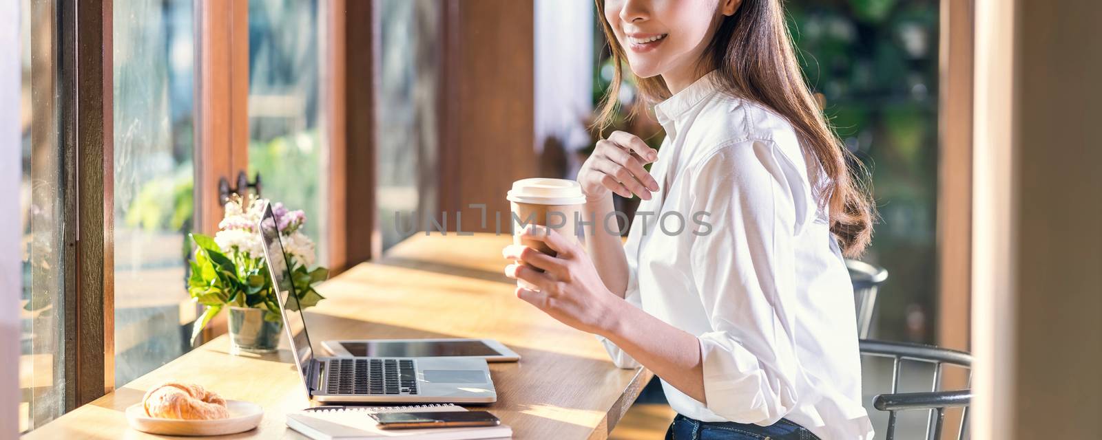 Banner of Portrait Young Asian woman holding and drinking a cup of coffee and working with technology laptop at a coffee shop.freelancer and entrepreneur working by connecting to internet via computer