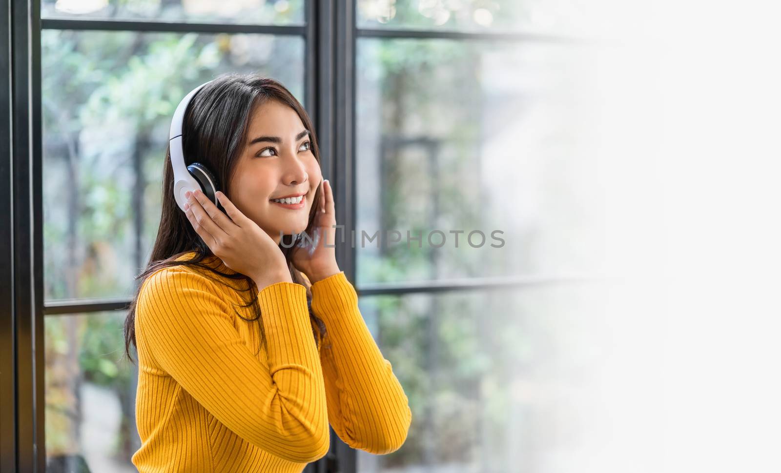 Happiness Asian smiling young woman wearing technology wireless headphones for listening the music via smart mobile phone in coffee shop or coworking space, Lifestyle and leisure with hobby concept