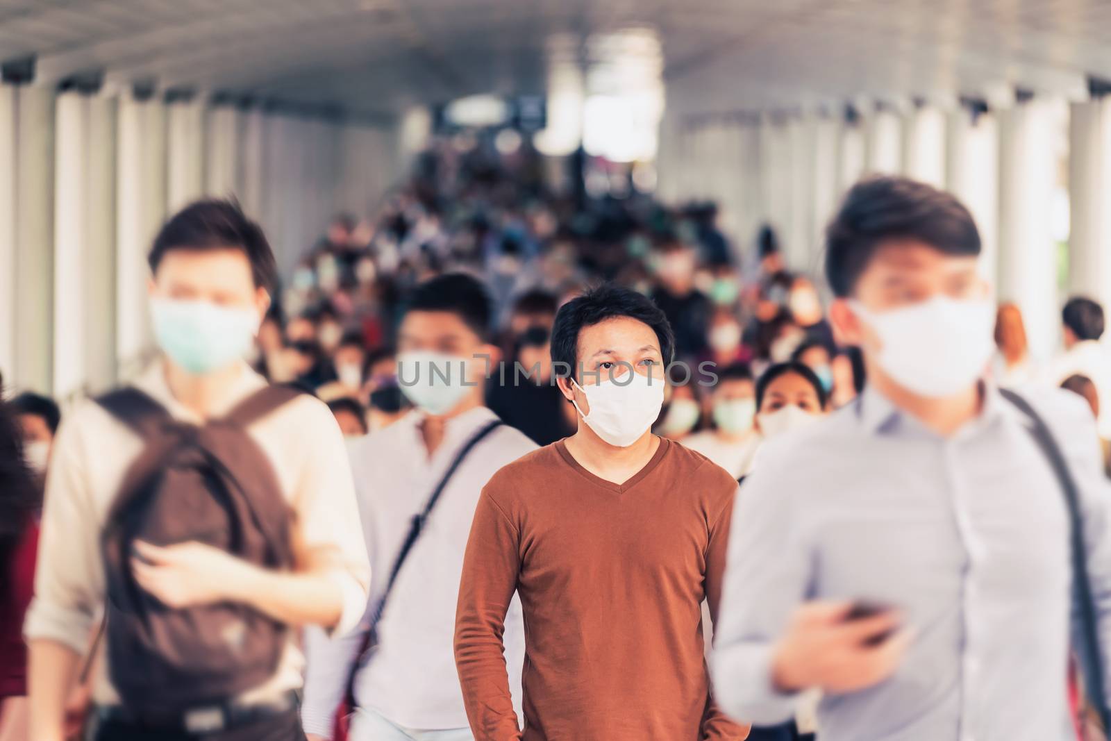 Asian man walking and standing between Crowd of blurred unrecognizable business people wearing surgical mask for prevent coronavirus Outbreak in rush hour working day at Bangkok transportation