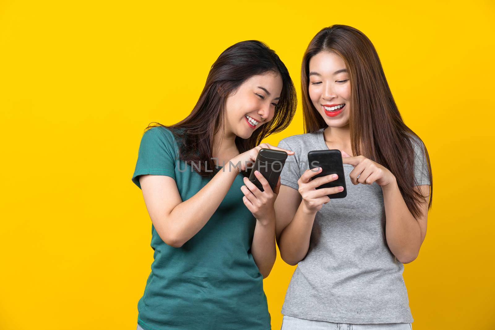 Two Happiness Asian smiling young woman gamer using smart mobile phone and playing games on isolated yellow color background, Lifestyle and leisure with hobby concept