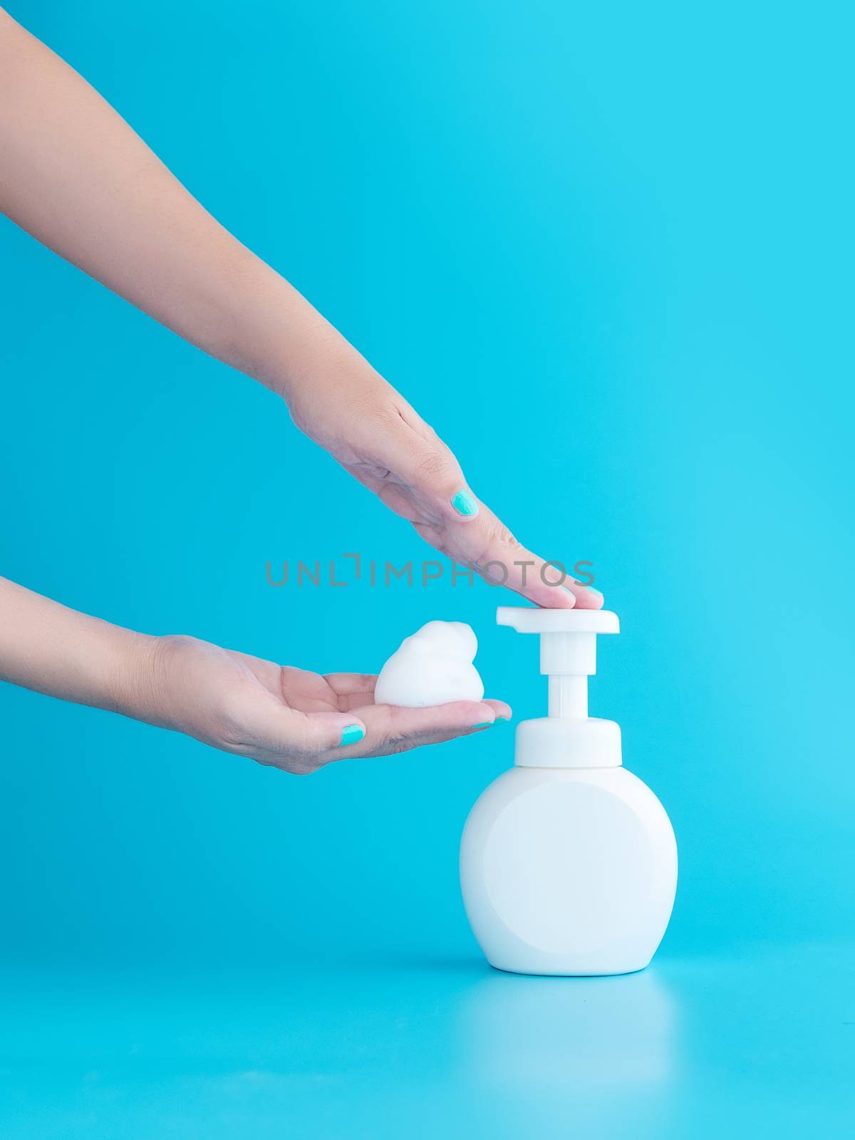 plastic pump bottle and mousse foam or cleansing foam on woman hand isolated on blue background, vertical with copy space. cleaning concept