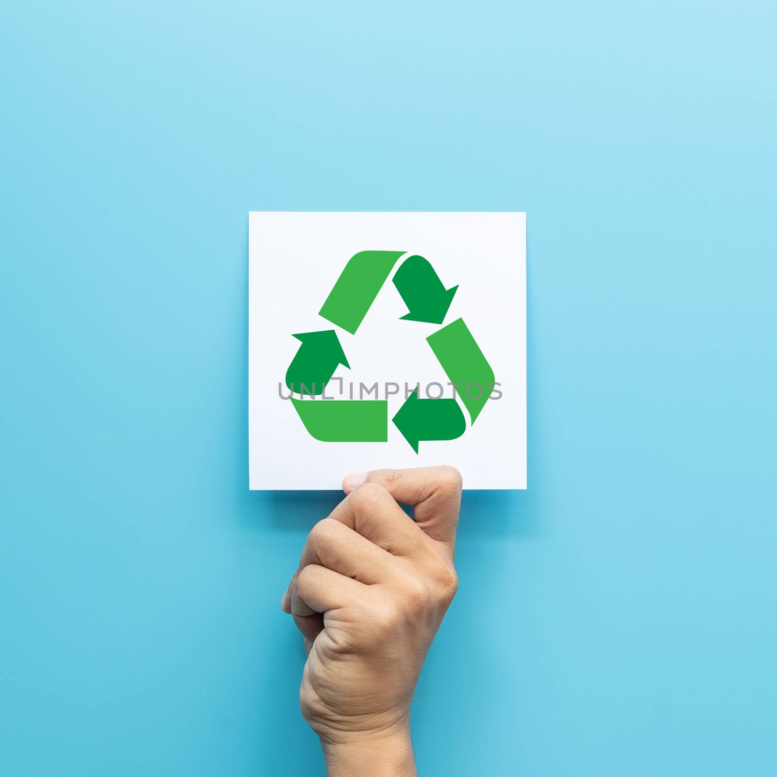 green recycling symbol on white paper card in hand isolated on blue background. green business concept for environment awareness  company