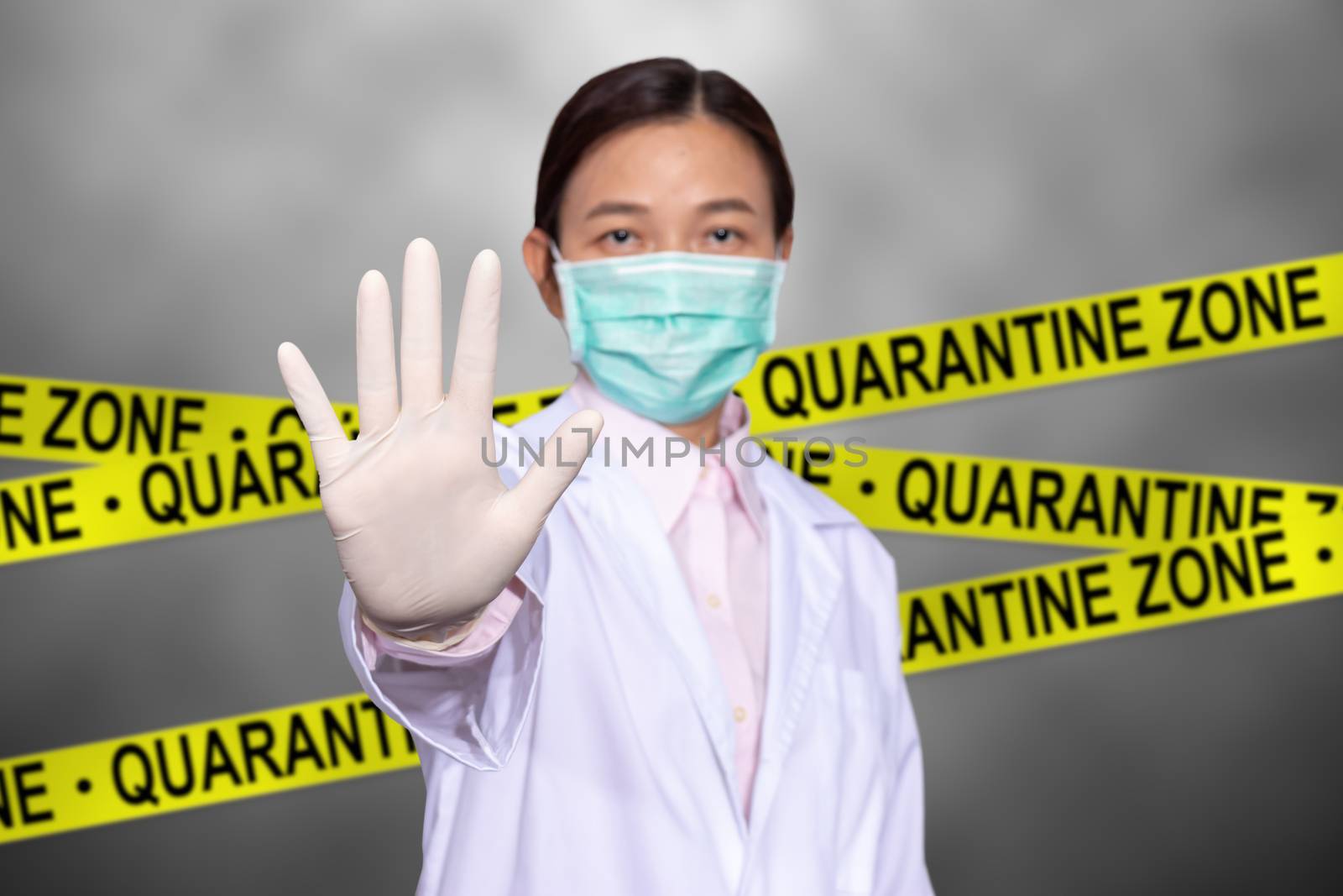 Asian female doctor wear a medical mask, raise hand for stop sign to do not enter quarantine area with yellow quarantine sign on the back, entrance is forbidden in quarantine zone.