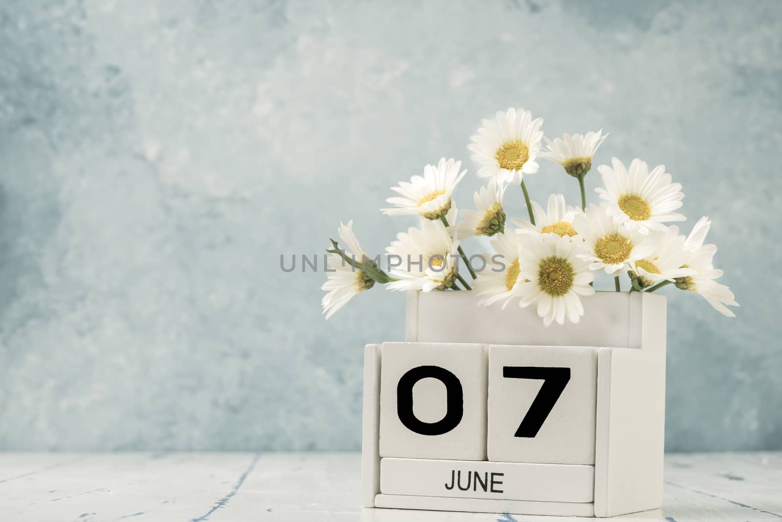 White cube calendar for june decorated with daisy flowers over blue background with copy space