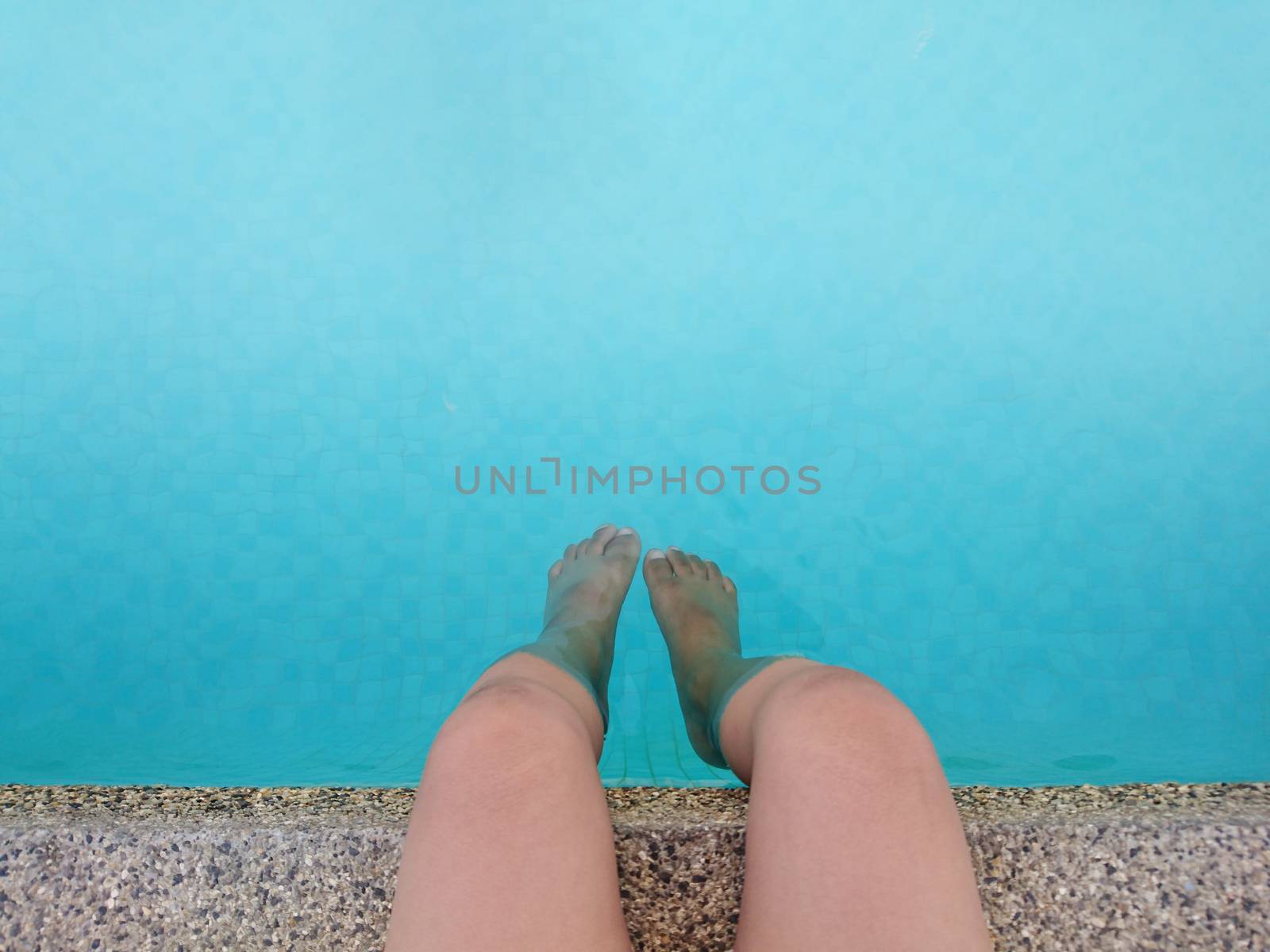 Little boy sitting legs down in the swimming pool