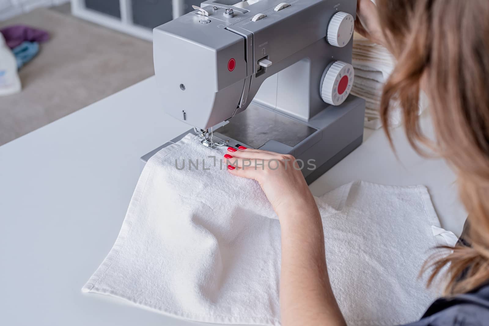 Woman sewing clothes at the sewing maching at home by Desperada