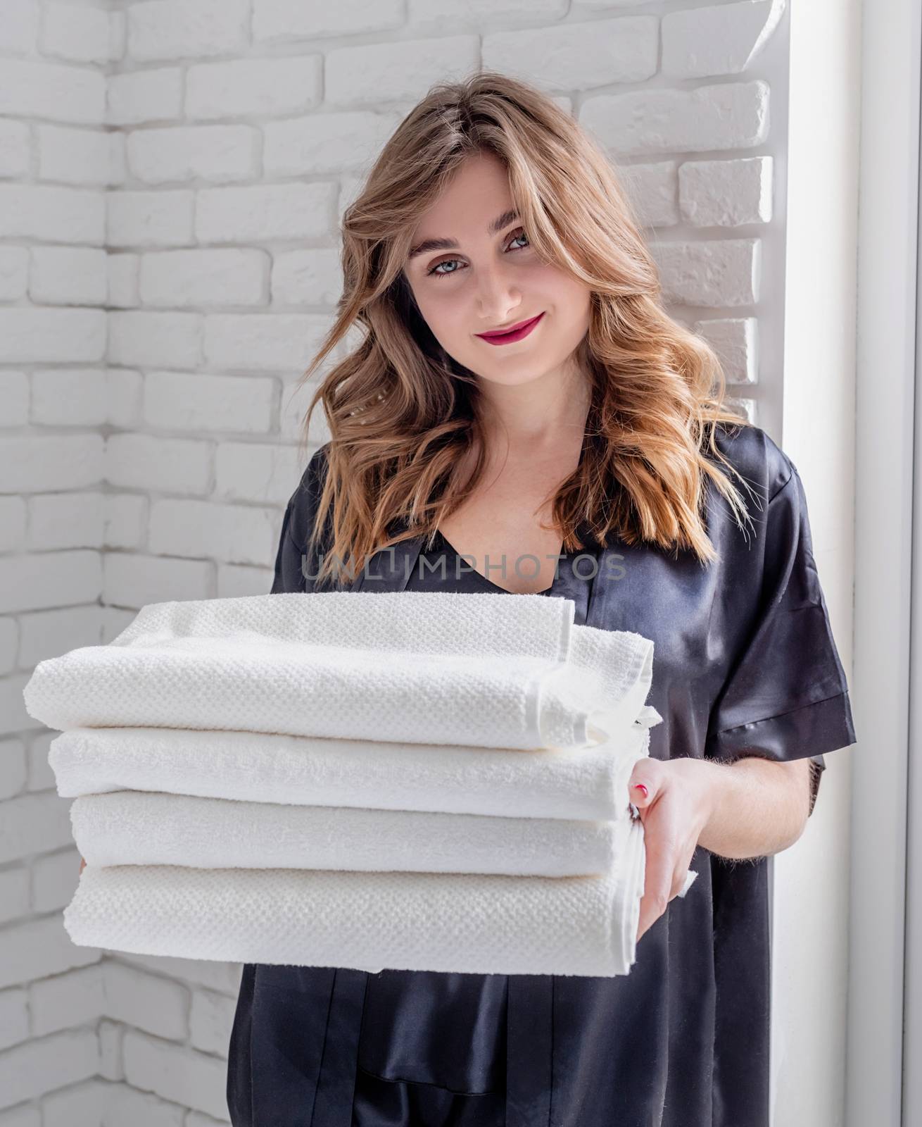 Laundry concept. Young beautiful woman in black pajamas holding a pile of clean white towels