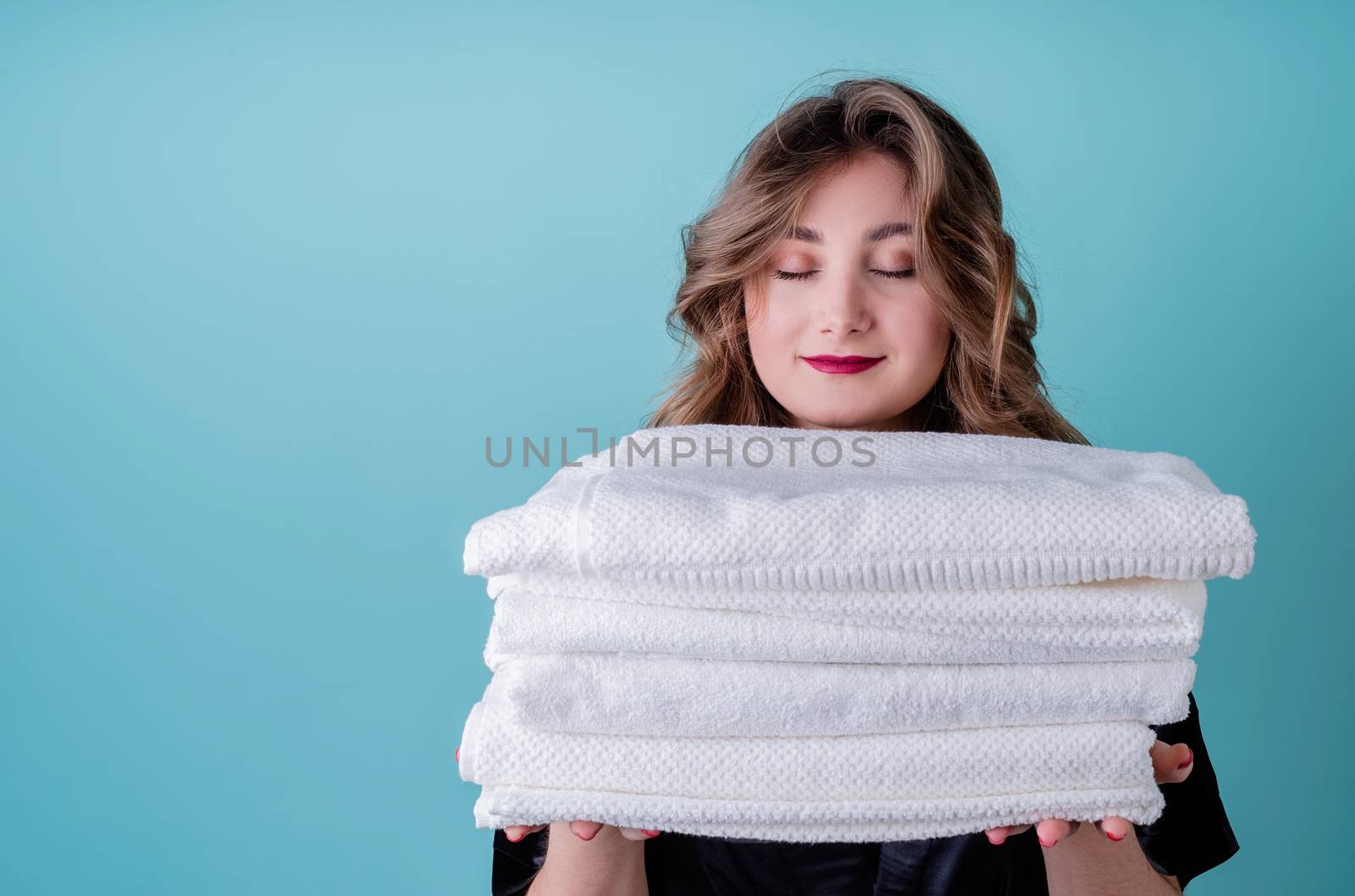 Laundry concept. Happy housewife holding a pile of clean white towels isolated on blue background with copy space