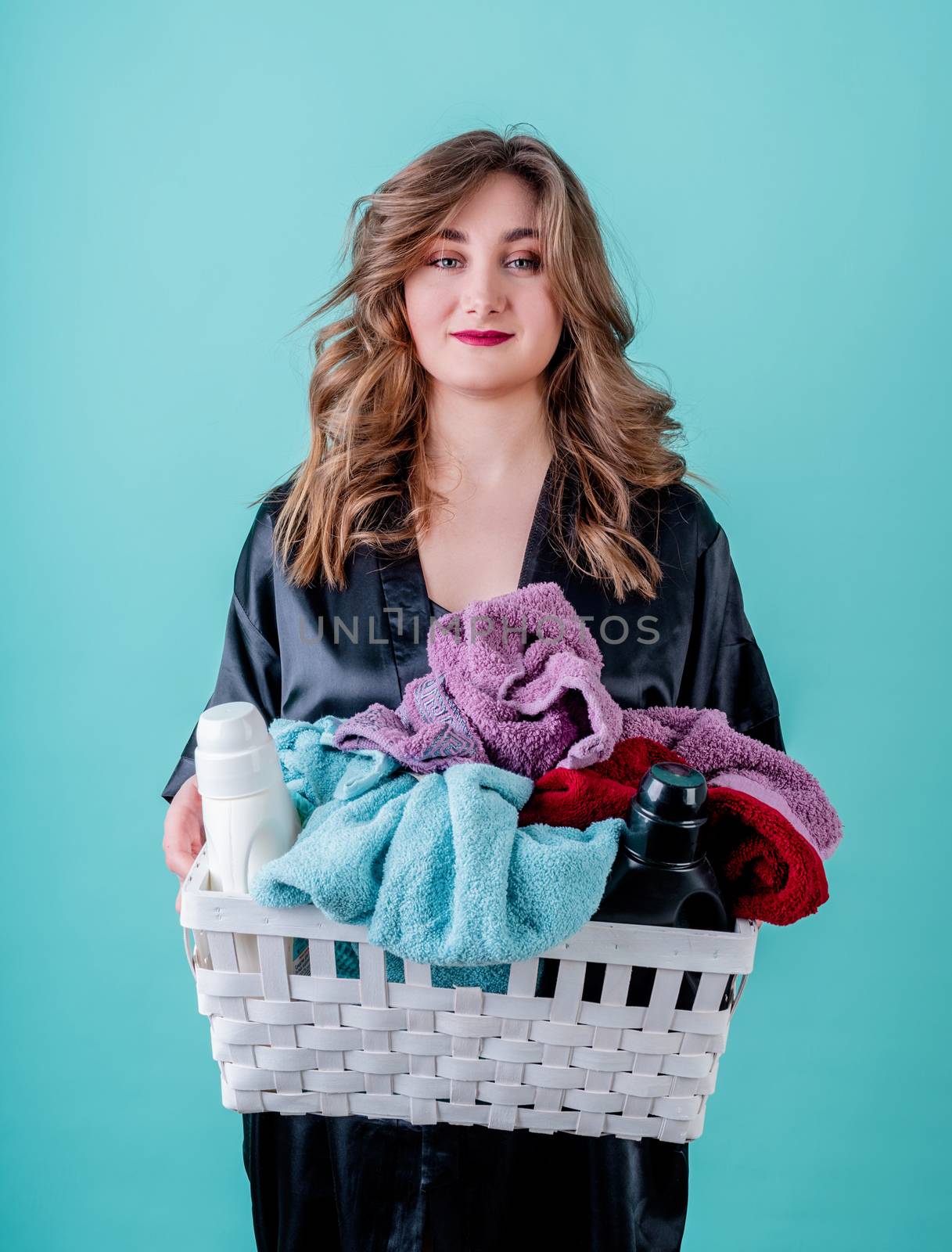 Laundry concept. Happy housewife holding a basket of clothes ready for laundry isolated on blue background