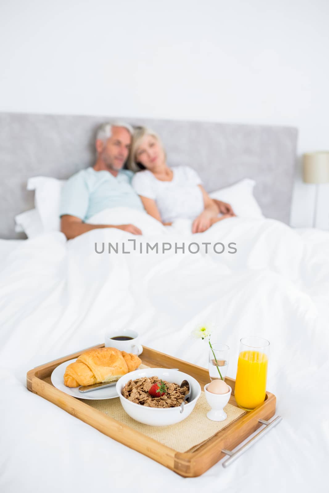 Couple sitting on bed with breakfast in foreground by Wavebreakmedia