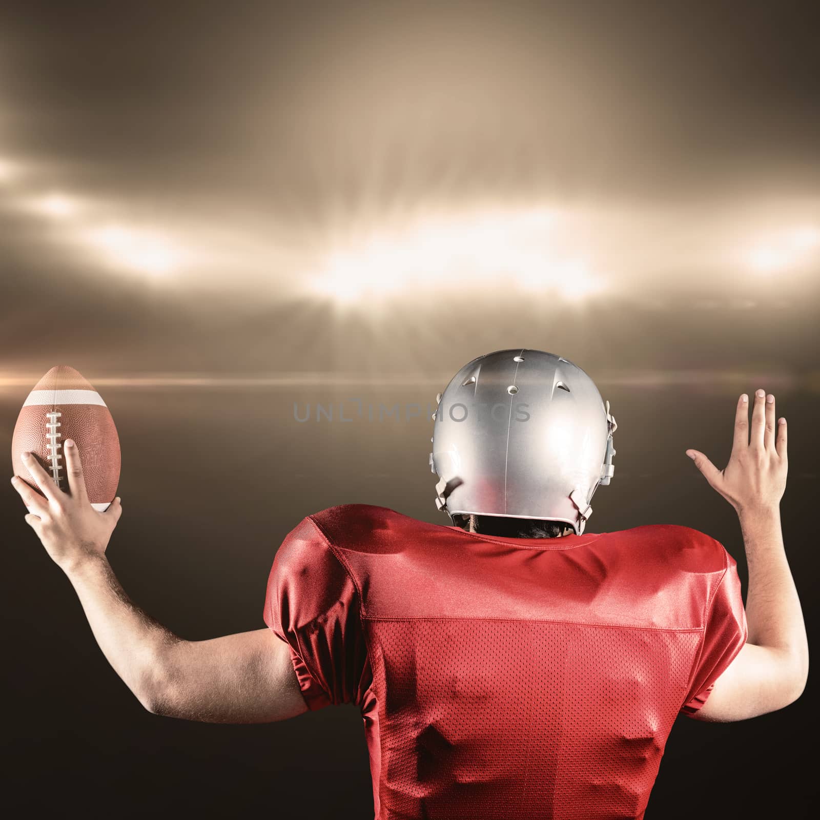 Rear view of American football player gesturing while holding ball against spotlight