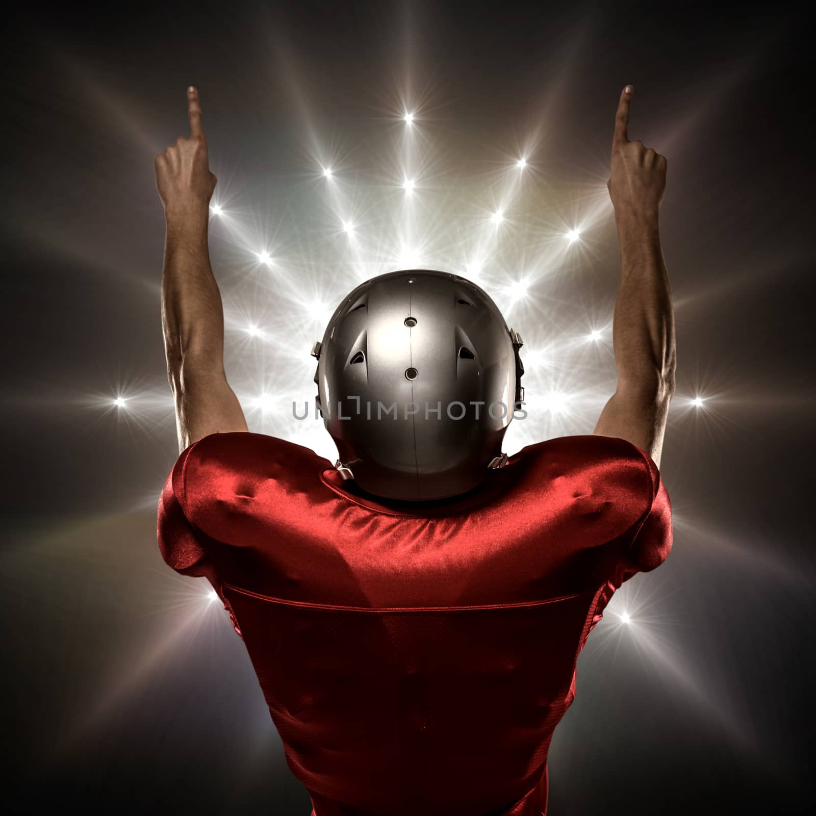 Rear view of American football player with arms raised against spotlight