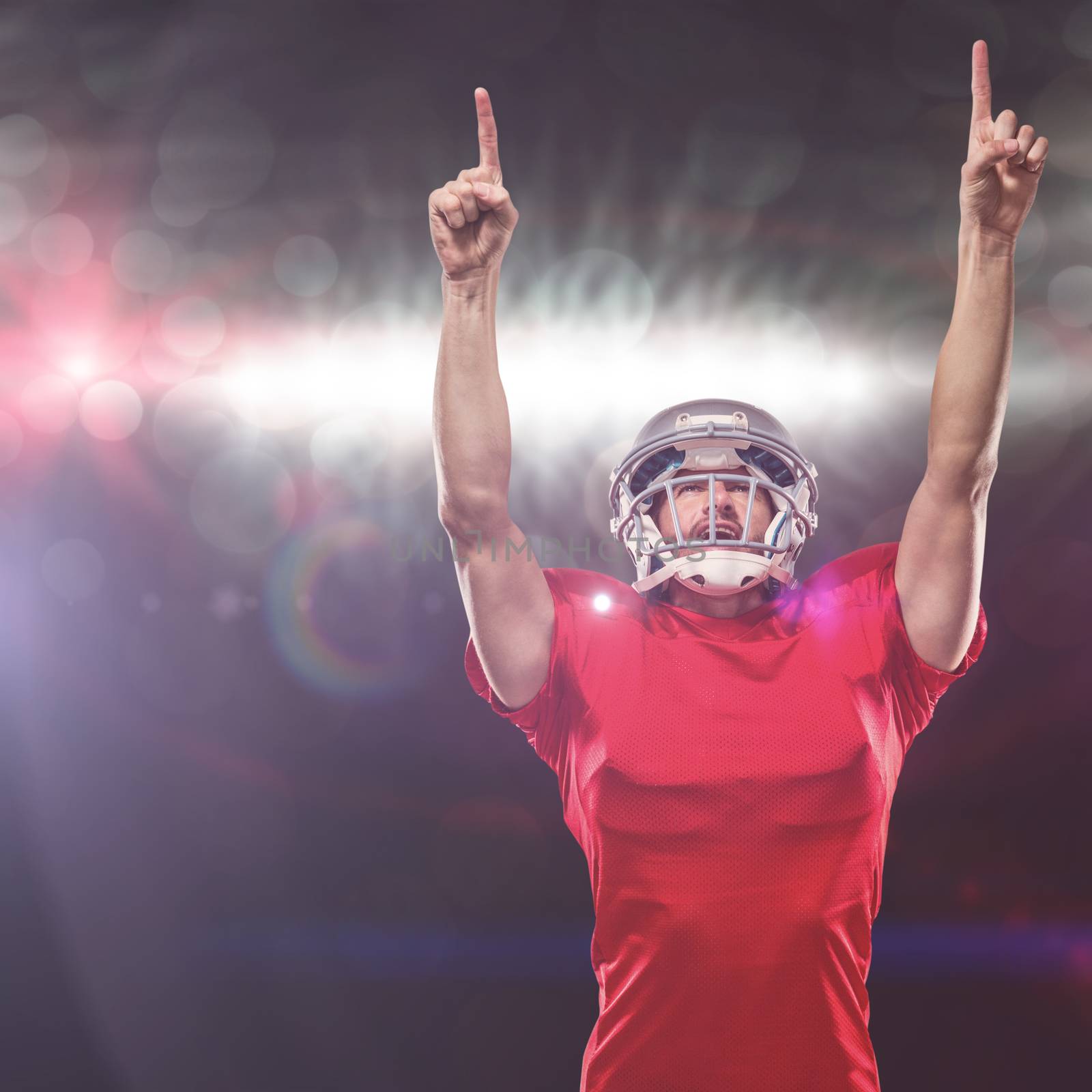 American football player looking up with arms raised against spotlights