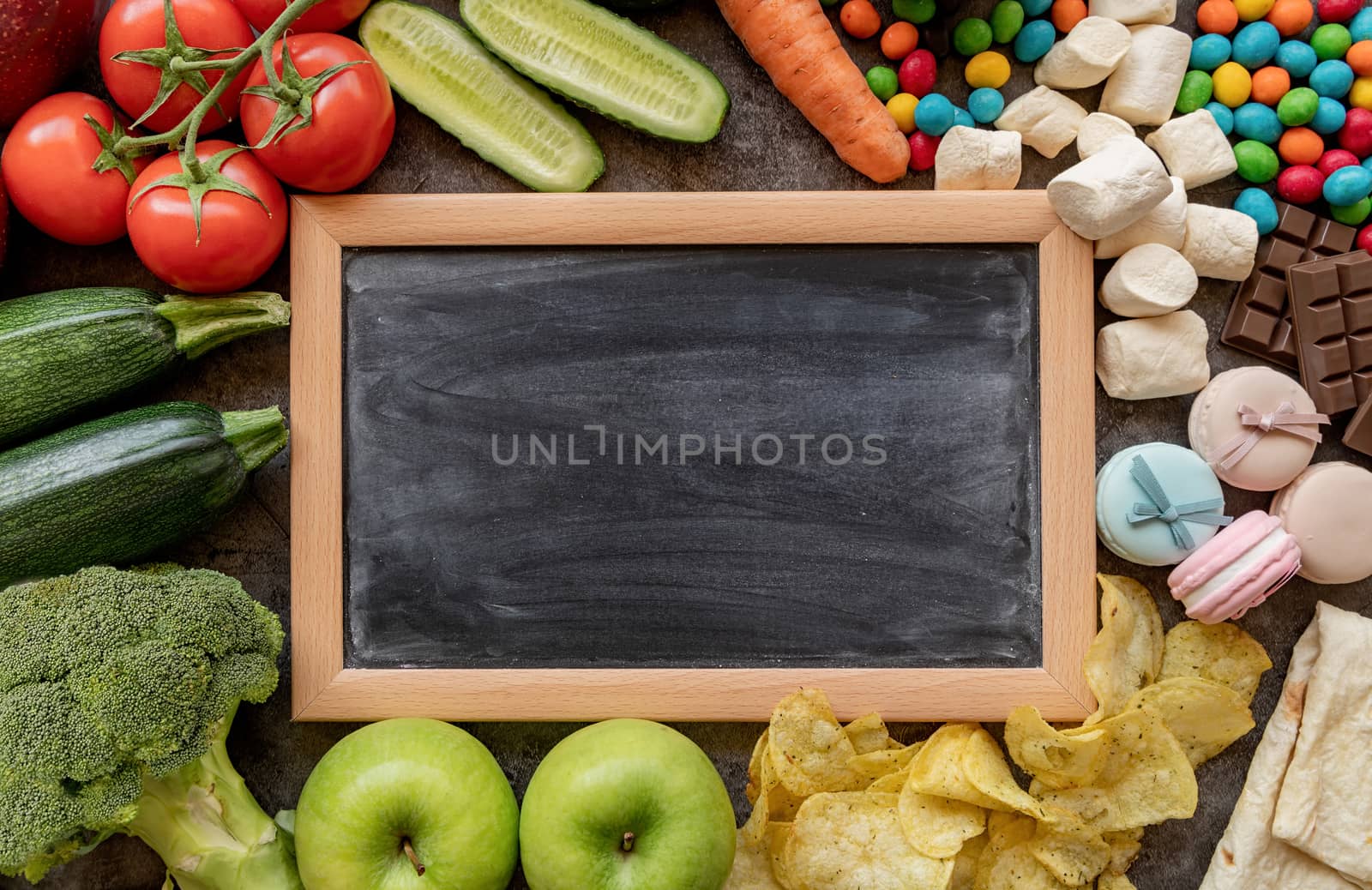 Fruit and vegetables vs sweets and potato fries around the blank chalk board top view flat lay by Desperada