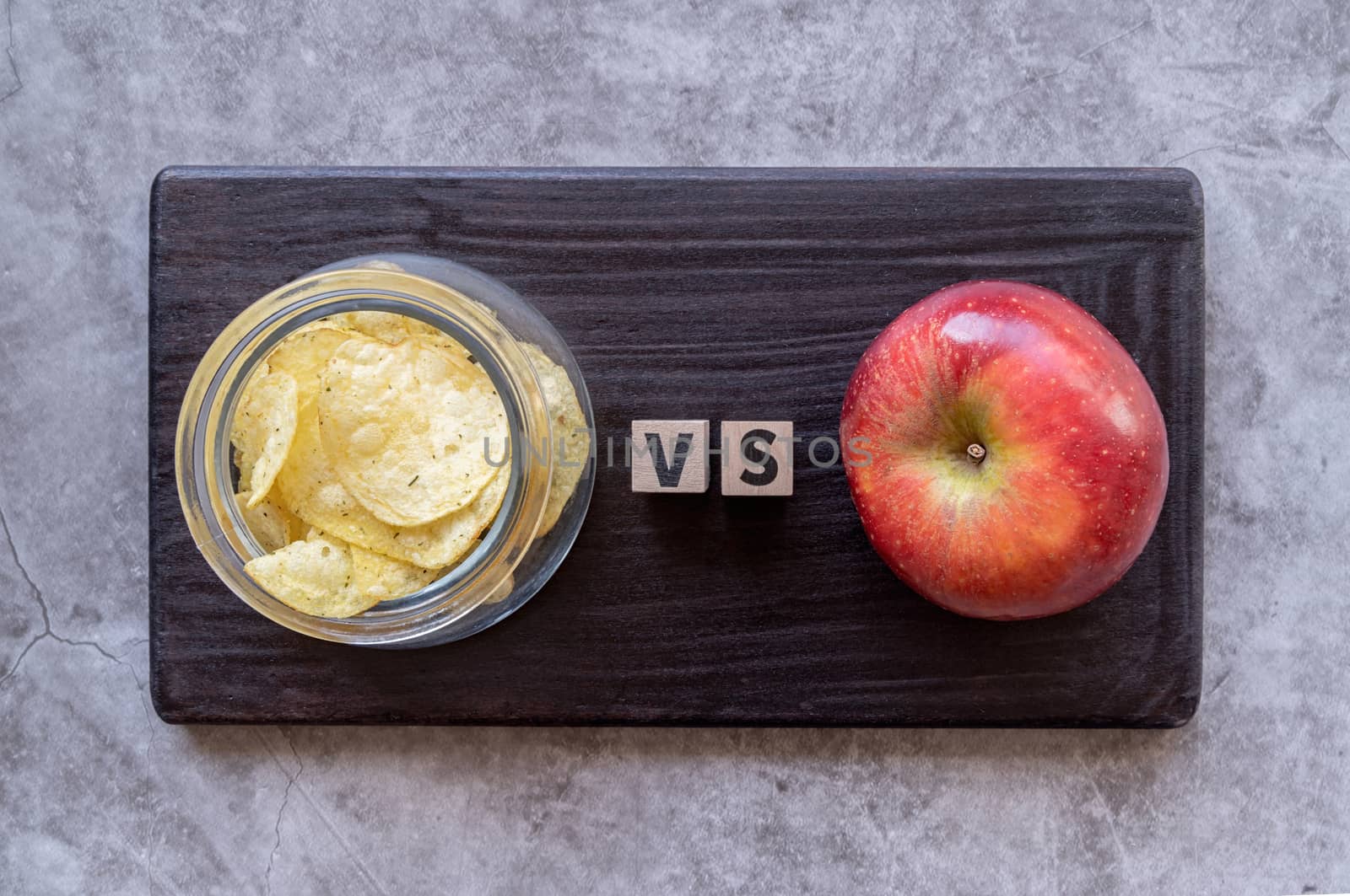 Healthy diet. Choosing between chips and apple top view on dark background