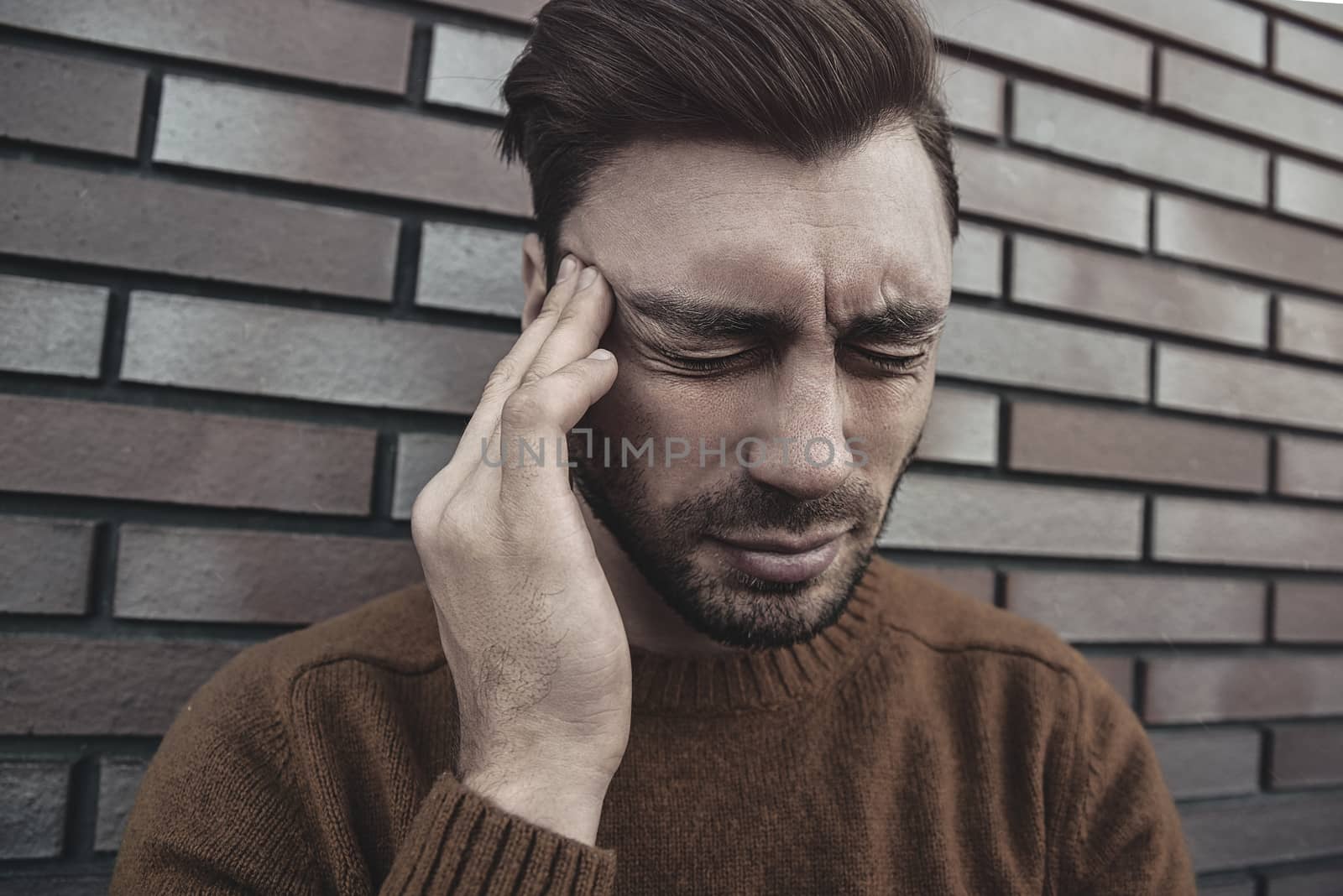 Man feeling painful emotions, screaming, witnessing death of close friend, being miserable and devastated, holding palms on head, yelling from pain and stress, standing unhappy over brown brick wall.